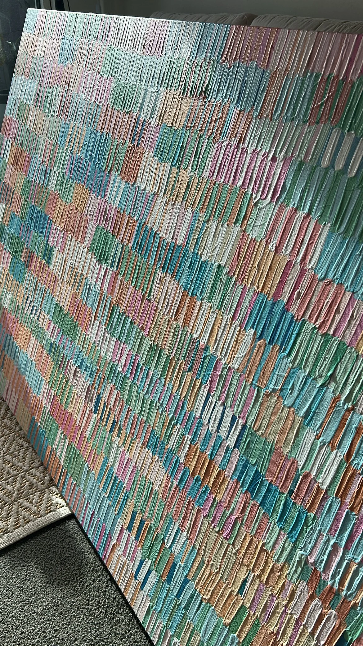 Close-up of an abstract textured painting with multicolored vertical and horizontal strokes in pastel shades of pink, blue, green, beige, brown, and white.