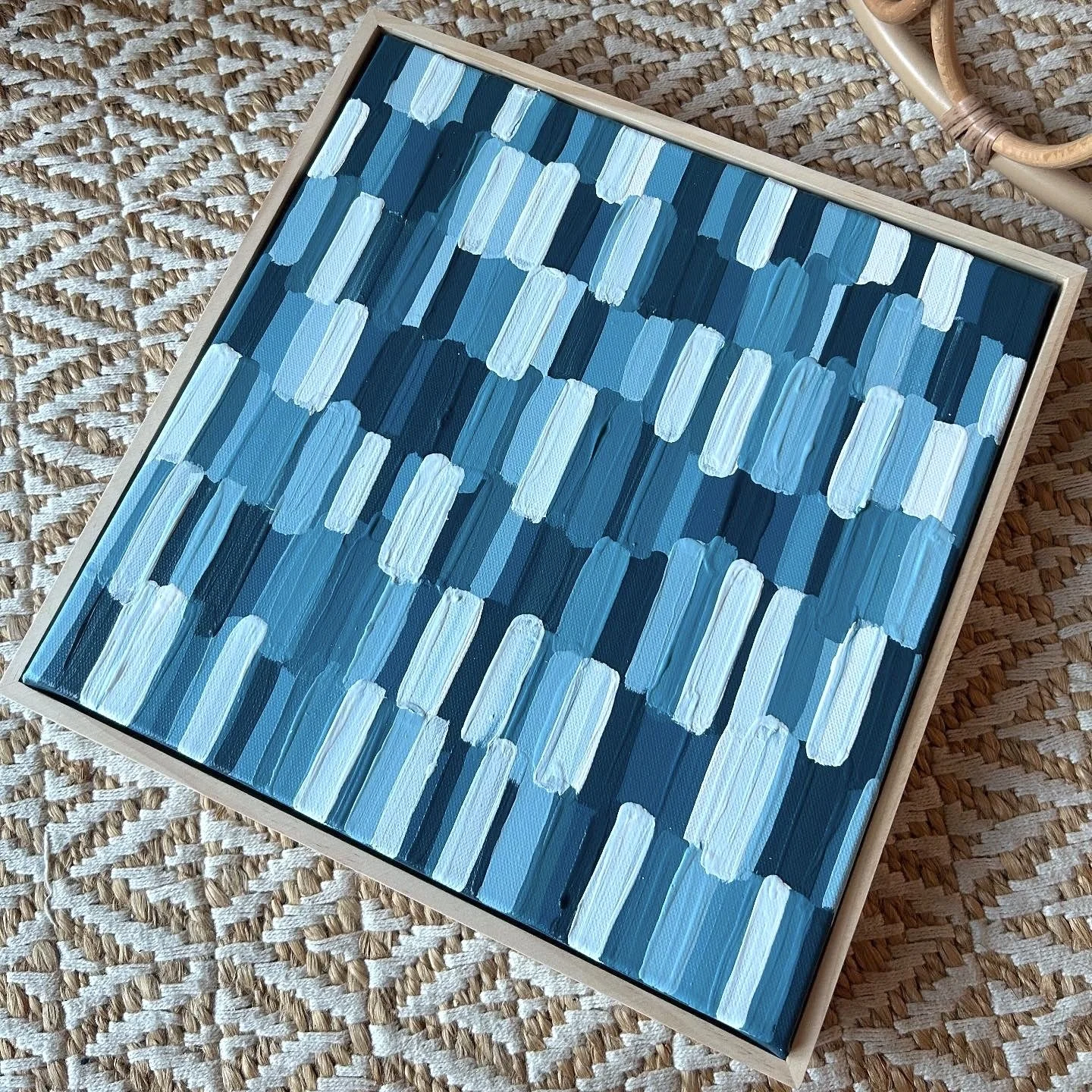 Abstract painting with various shades of blue and white brushstrokes framed in a light wooden frame.