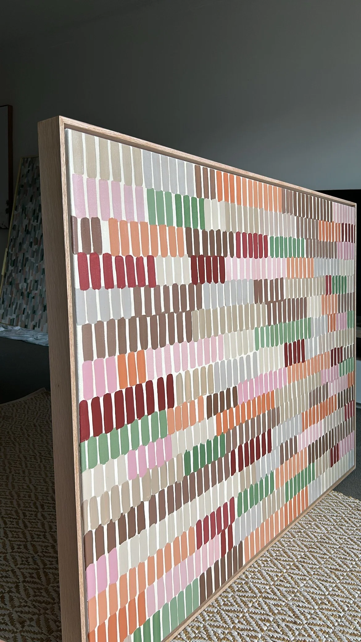 A large wooden frame with rows of colorful paint samples or fabric swatches arranged systematically in various shades of pink, green, brown, beige, white, and red.