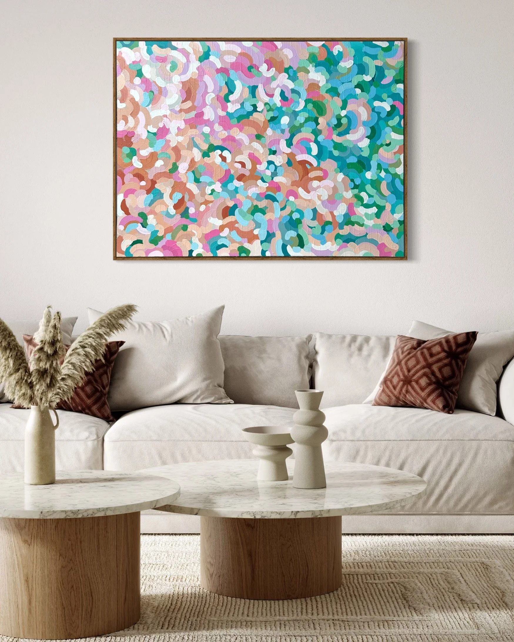 Living room with a white sofa, beige cushions, two brown cushions, a marble-top coffee table with decorative white ceramic vases, and a colorful abstract painting hanging on the wall.