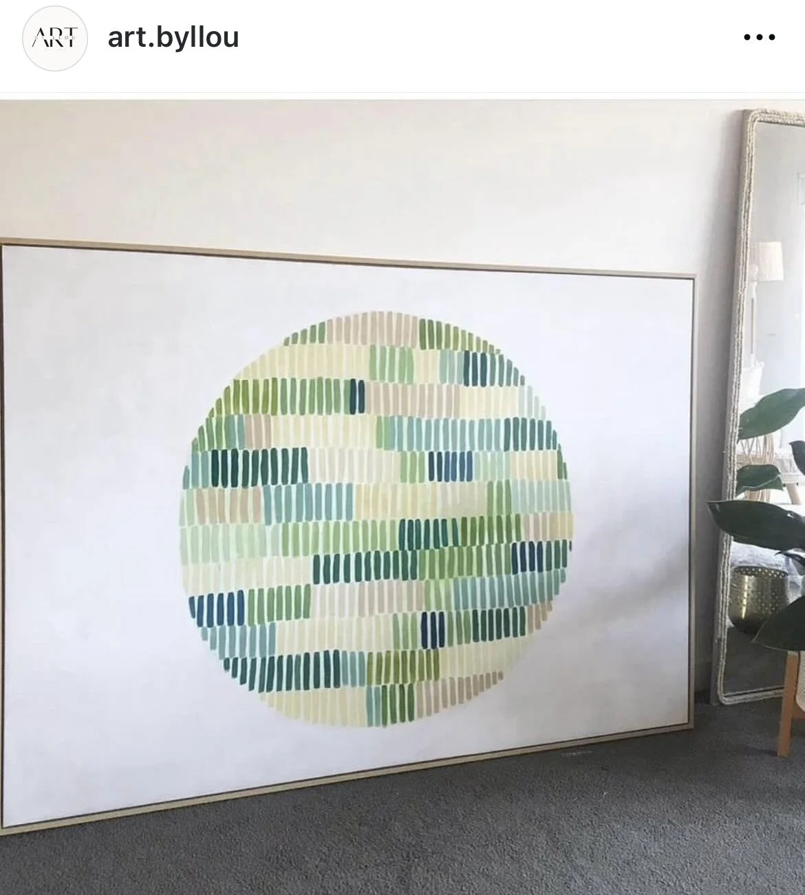 Colorful abstract artwork with horizontal rectangular brushstrokes in various shades of green, blue, beige, and cream, arranged in a large circle on a white background, displayed on a wall in an indoor setting.