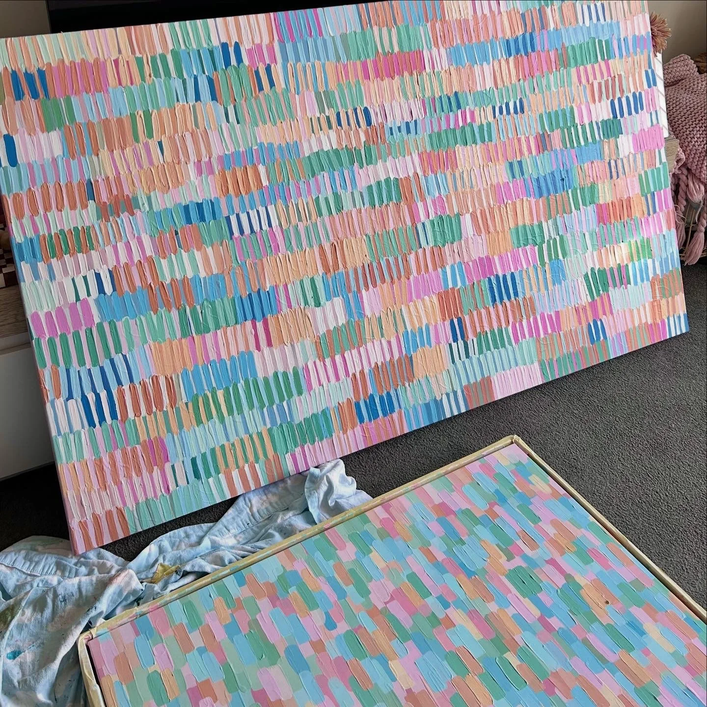 Two large colorful abstract paintings with streaks of pastel colors leaning against each other in an indoor setting.