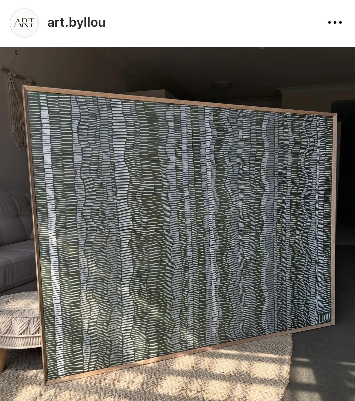 A framed modern abstract artwork with wavy black and white horizontal lines behind a transparent curtain on a beige carpet in a living room.