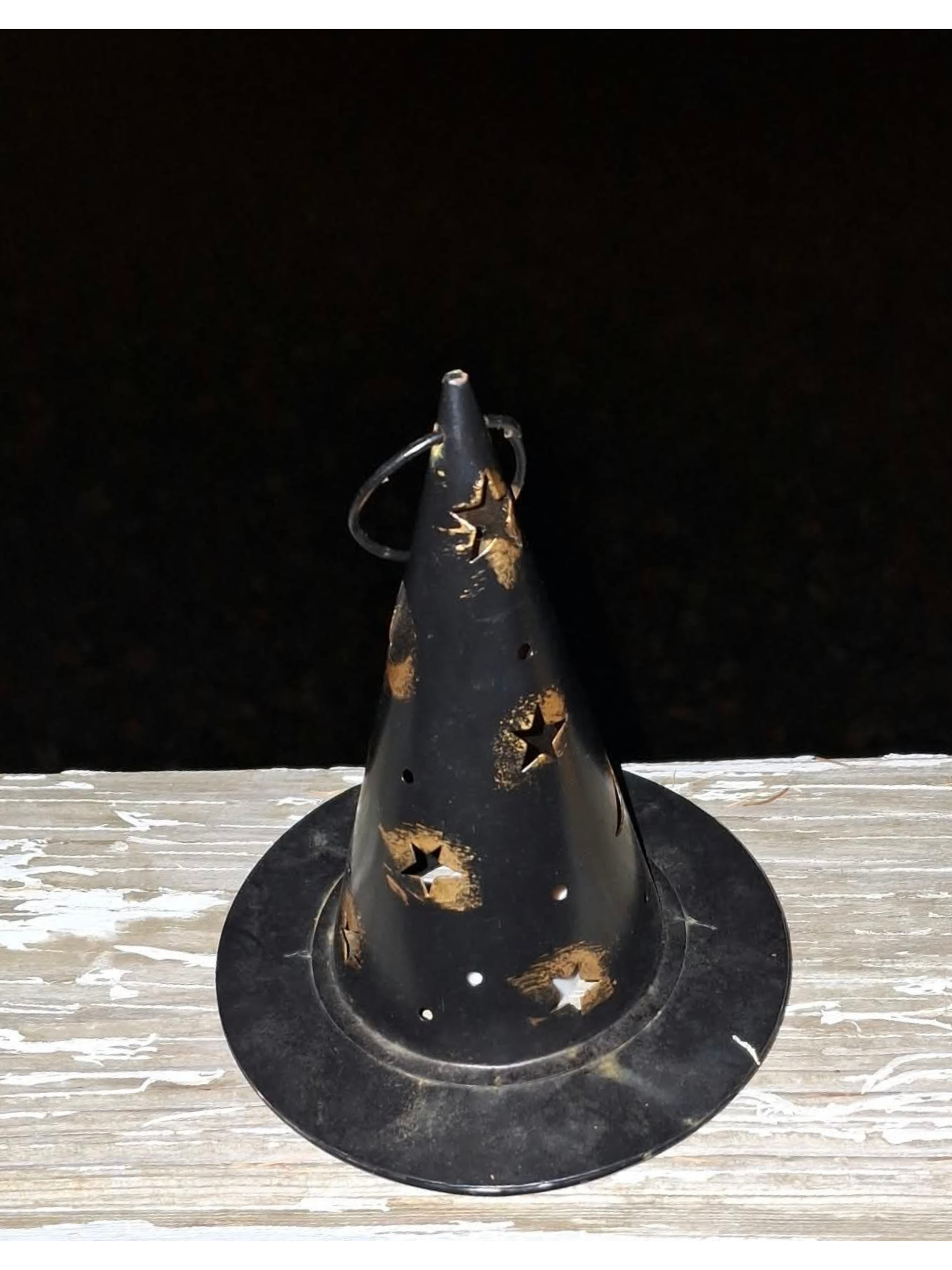 Metal witch hat Halloween decoration sitting on a wooden surface with a dark night sky behind it.