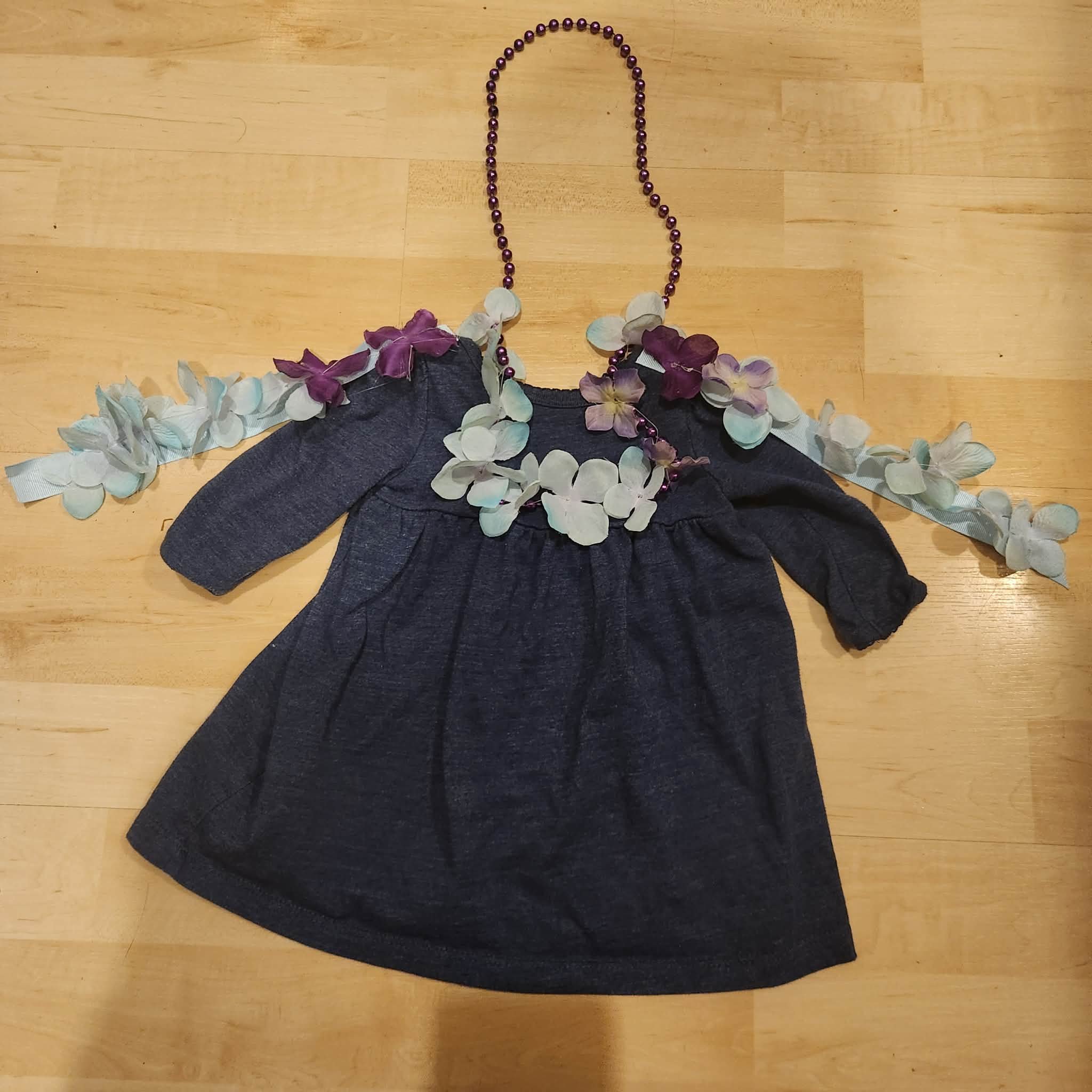 Toddler costume with artificial flowers and optional beads on a wooden floor.