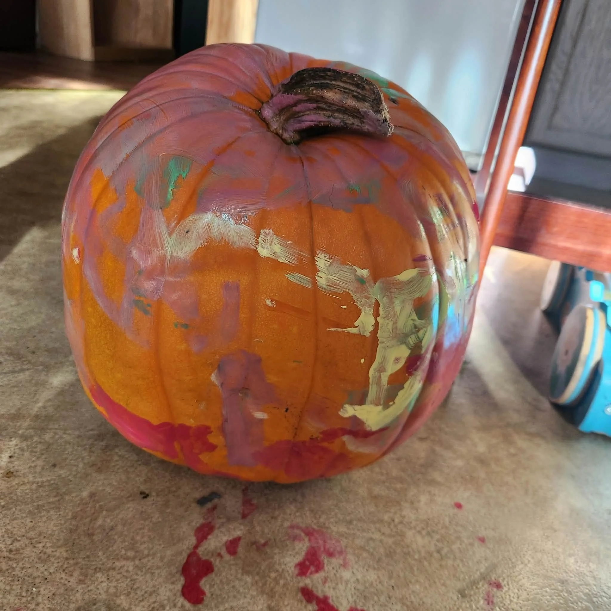 A pumpkin sitting on the floor with purple, yellow, red, and green paint smeared on it.