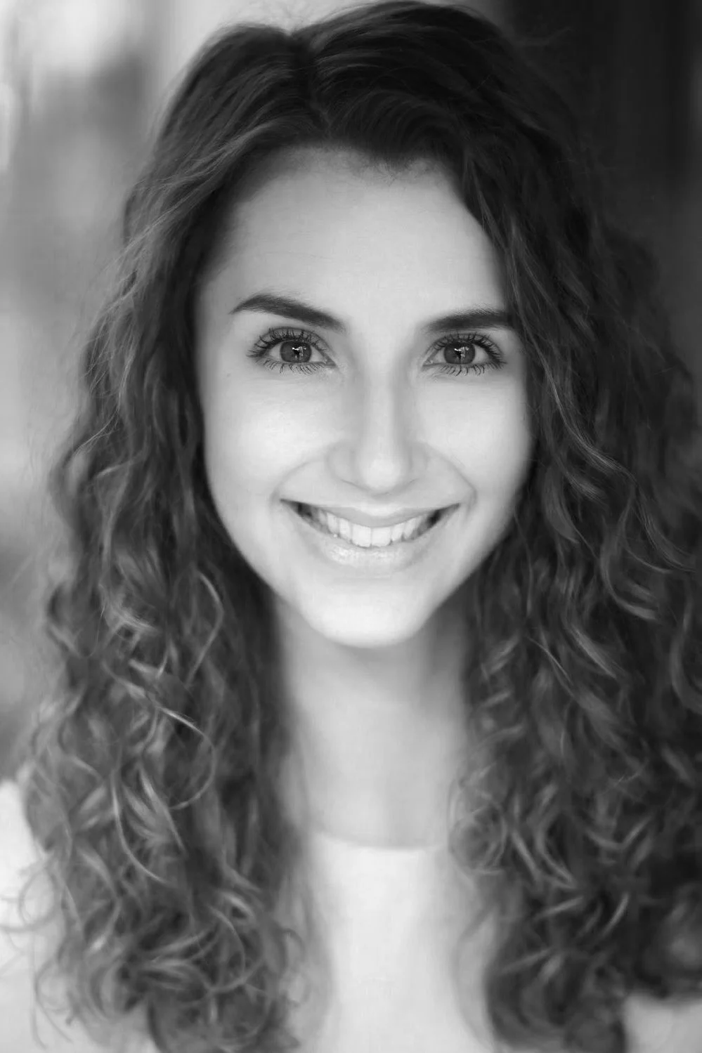 Black and white close-up photo of a woman with curly hair smiling at the camera.