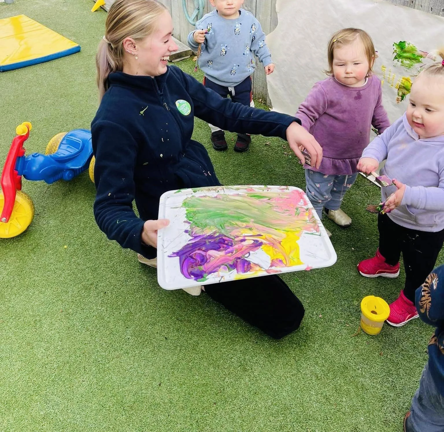 A teacher and toddlers enjoying a messy art session outside at Happy Days Childcare, exploring colour and creativity through hands-on learning.