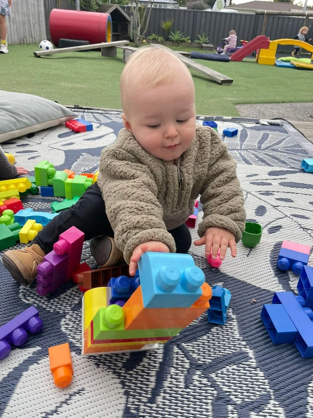 Infant playing with large colourful building blocks during outdoor playtime at Happy Days Childcare, Taradale