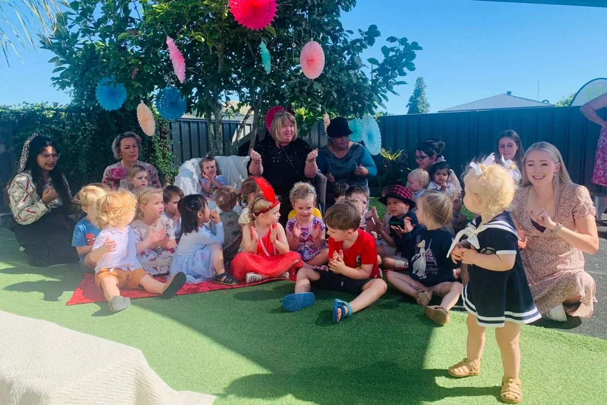 Tamariki dressed up for a celebration at Happy Days Taradale, enjoying music, connection and creativity with teachers under a tree filled with decorations.