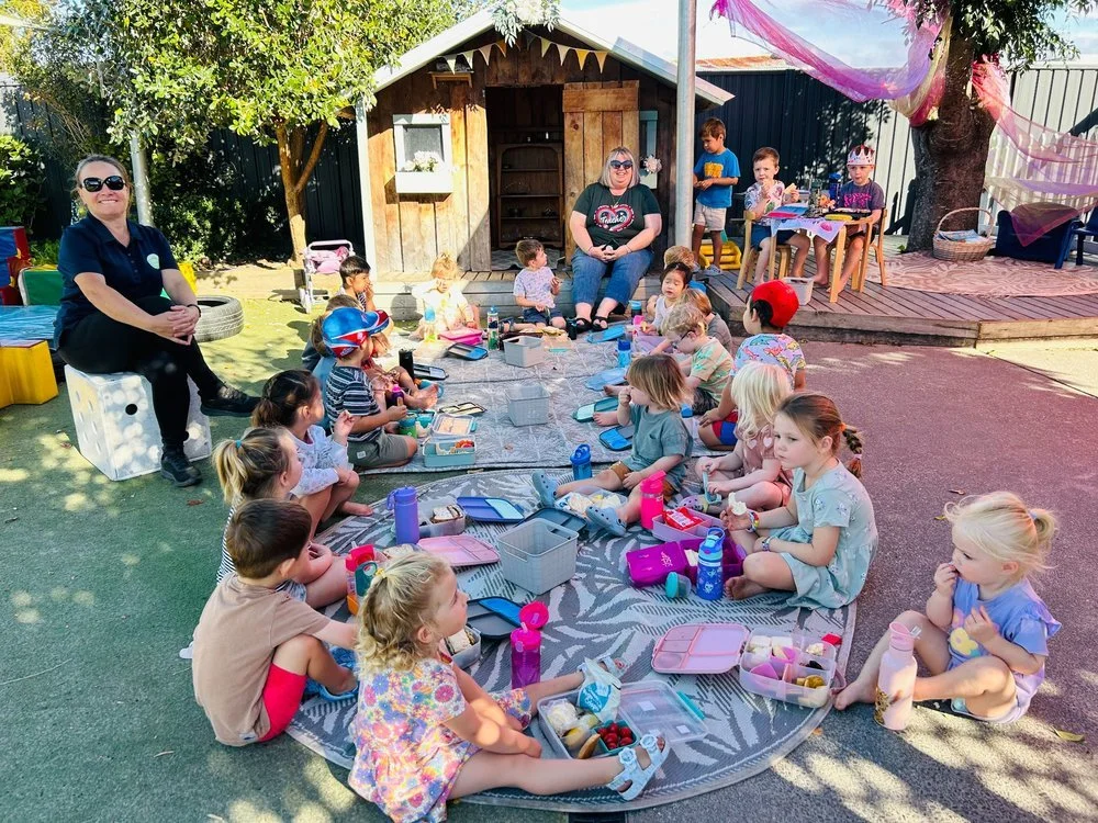 Group of preschool children enjoying a shared picnic lunch outdoors with teachers at Happy Days Early Childhood Centre