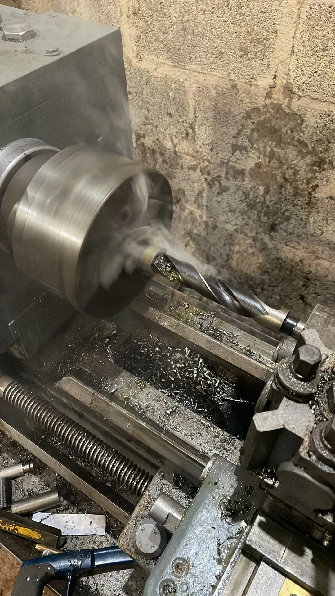 Metal lathe machining a piece with a drill bit, surrounded by metal shavings