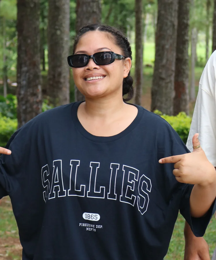 A young woman in sunglasses and a Sallies T-shirt, smiling
