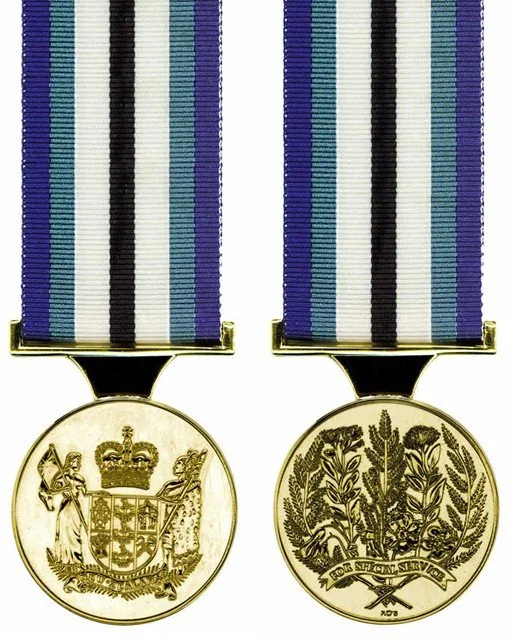 Two gold medals with blue, black, white, and green striped ribbons side by side, each featuring different designs on their front faces.