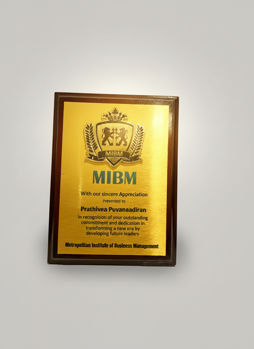 A framed gold-colored plaque with black text and a crest at the top, awarded by the Metropolitan Institute of Business Management to Prathiva Puvanaadiran for outstanding dedication and leadership.