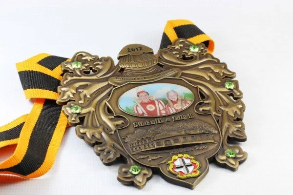 A bronze medal with a black and yellow striped ribbon, featuring a portrait of two children, a train, and a shield with a red cross.