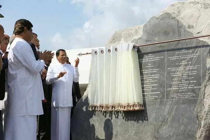 Indigenous leaders and officials unveiling a plaque at a memorial site during daytime with cloudy sky.