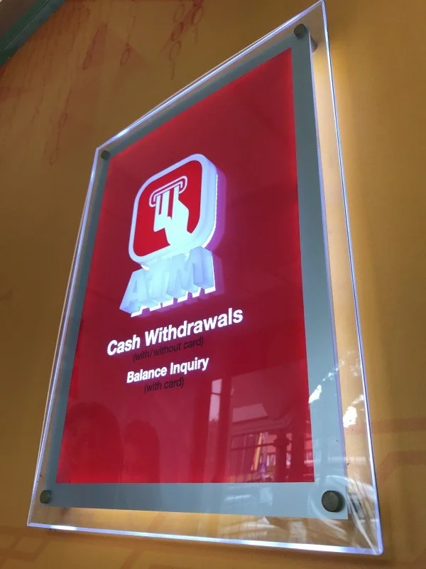 A digitally lit sign with a red background displays services for cash withdrawals and balance inquiries at an ATM, with instructions for usage including card requirements.