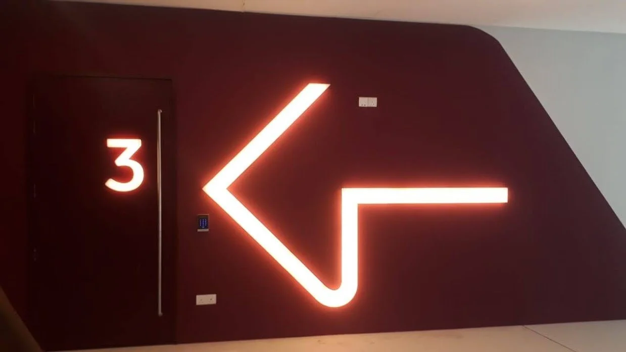A dark red wall with a bright red illuminated left arrow sign and a white number 3 on a door.