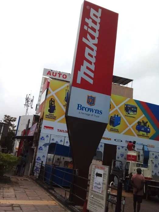 Tall signboard advertising Traktil and Browns with a background of a hardware store and people walking nearby.
