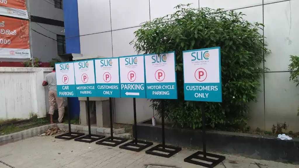 A row of parking signs for car and motorcycle parking, and customer-only parking, placed in front of bushes and a wall with a person standing nearby.