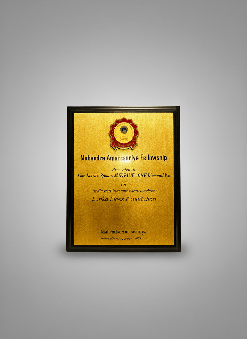 A gold-colored plaque with a black frame and a badge at the top. The plaque is awarded to Lion Deniek Symaas MaE, PILOT - ONE Diamond Piu, for dedicated humanitarian services to the Lanka Lions Foundation, presented by Mahendra Amarasuriya in 2007.