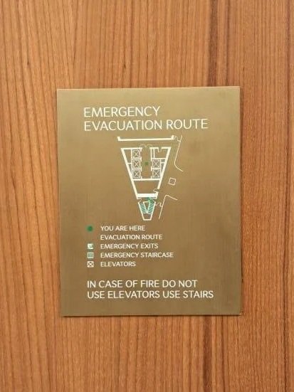 Emergency evacuation route sign on a wooden wall indicates the path to safety, with symbols for evacuation route, emergency exits, emergency staircase, and elevators, and a note not to use elevators during fire.