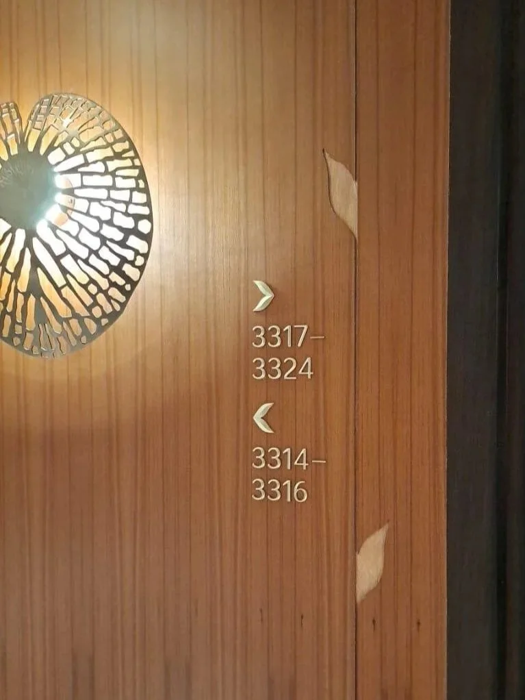 Room directional signs on a wooden wall with metal symbols and room numbers 3317, 3324, 3314, and 3316.