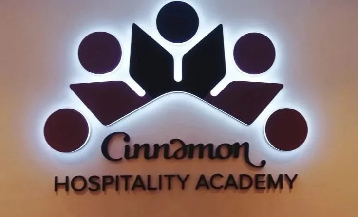 Logo of Cinnamon Hospitality Academy featuring a stylized flower with five circular petals surrounding a central dot, with the words 'Cinnamon' and 'Hospitality Academy' underneath.