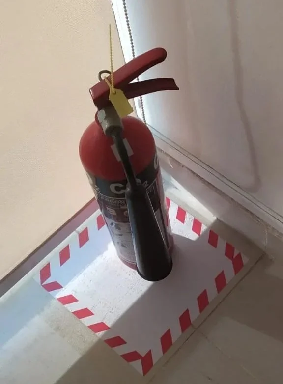 A fire extinguisher hanging from a electrical cord inside a red and white striped box.