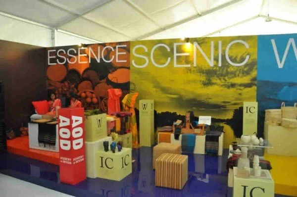Display booth with colorful banners reading 'ESSENCE,' 'SCENIC,' and other text, showcasing various packaged products and promotional materials.