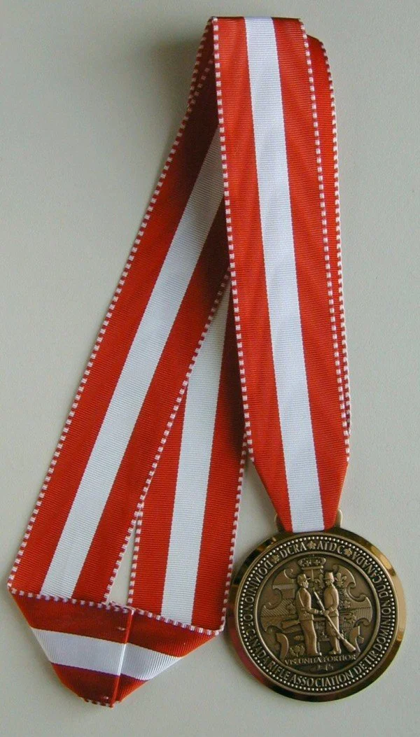 A bronze medal with a red and white striped ribbon, featuring an engraving of two people shaking hands and German inscriptions.