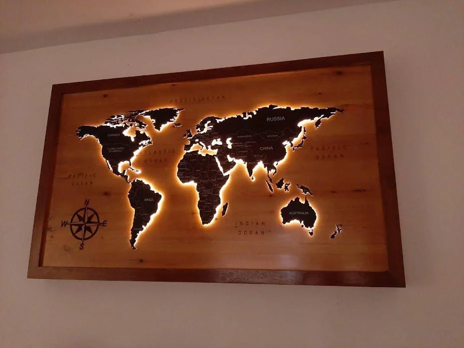 Wooden world map with country names and backlit illumination, including a compass rose in the bottom left corner.
