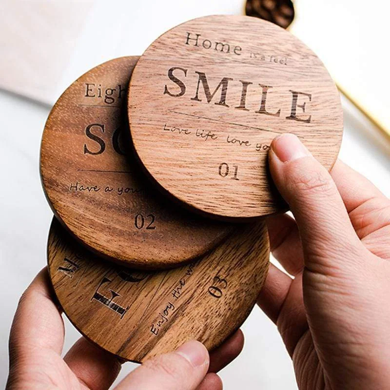 Three round wooden coasters with engraved motivational words and phrases, held in hands.