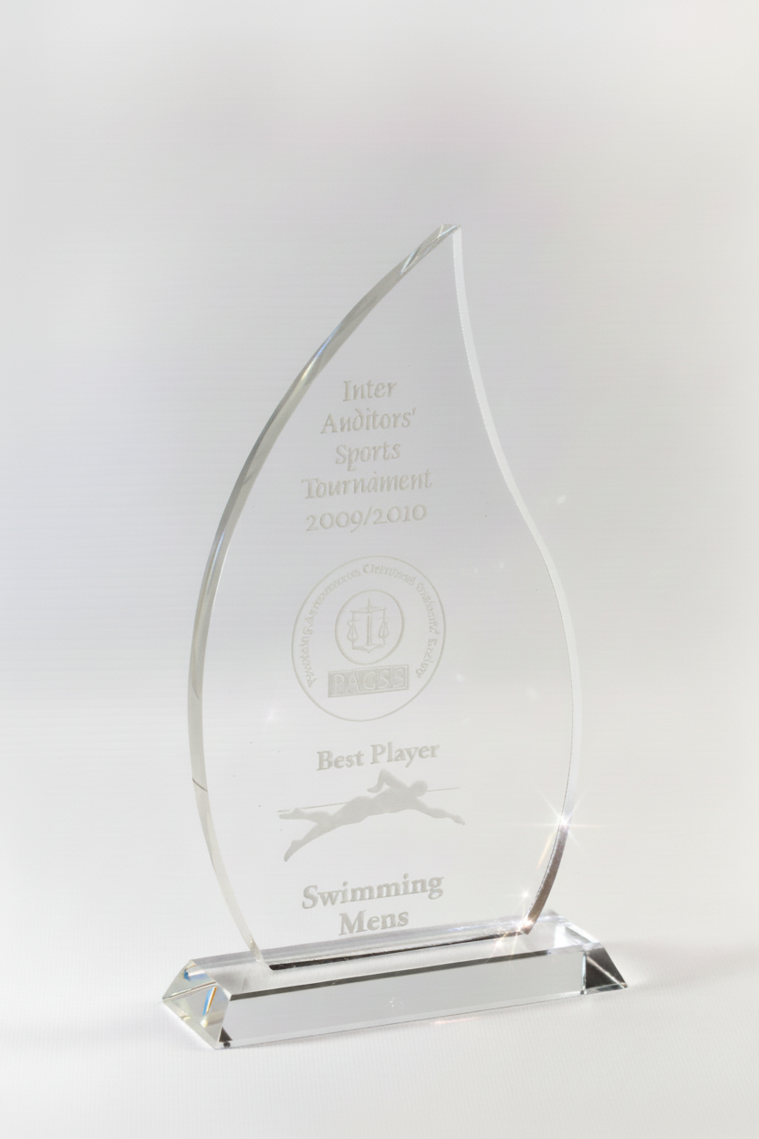 A clear, teardrop-shaped glass award with an engraved inscription honoring a men's swimming tournament from 2009-2010, awarded for best player.
