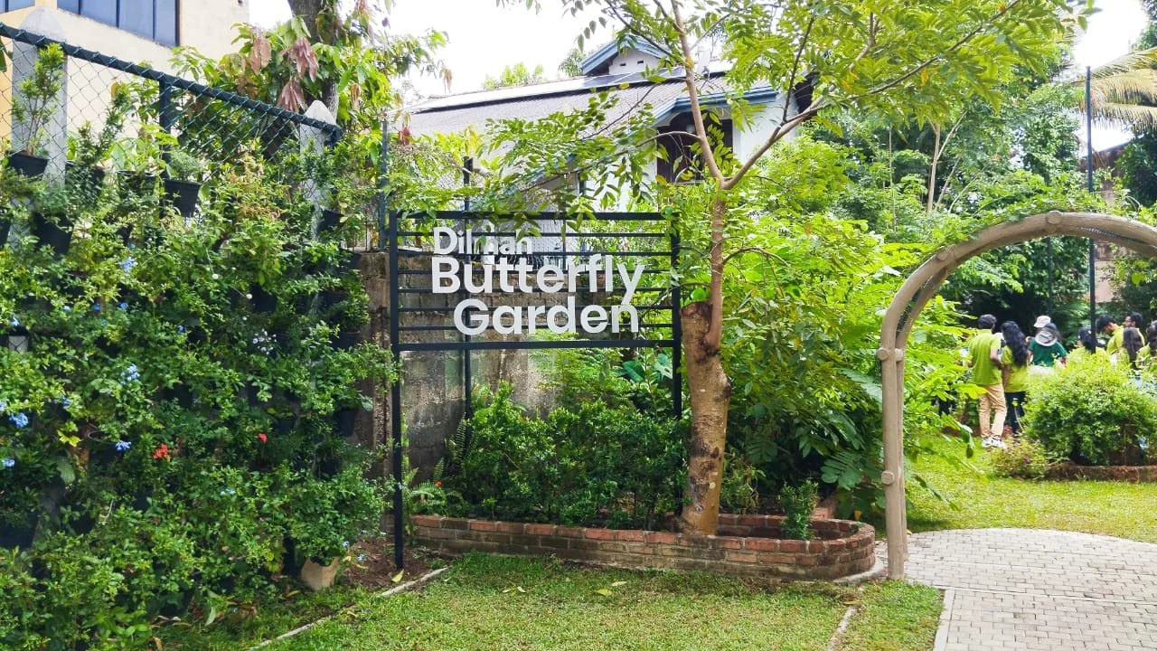Entrance to Diman Butterfly Garden with lush greenery, trees, and a group of people in the background.