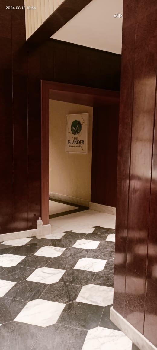 Interior view of a building with dark wood paneling, marble tile flooring in a checkerboard pattern, and a partially visible sign for 'The Islander' restaurant or establishment on the wall in the background.