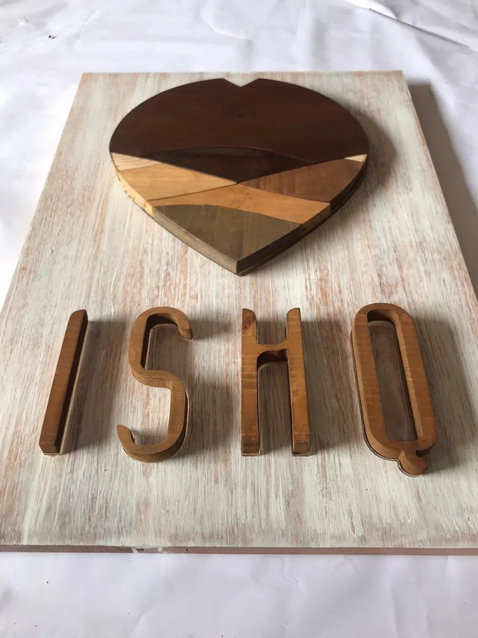 A wooden heart-shaped plaque with geometric patterns and the word "LOVE" spelled out in wooden letters, placed on a light-colored wooden surface.