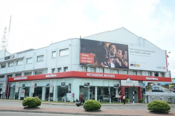 A Mitsubishi Motors dealership on a street corner with a large HSBC advertisement on the upper floor showing a family and a red banner with the Mitsubishi logo.