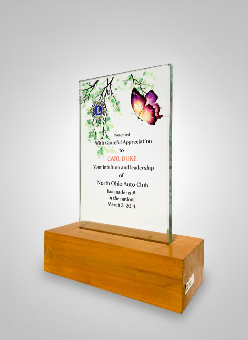 A clear glass plaque with colorful flower and butterfly illustrations, mounted on a wooden base, presented as an appreciation award to Carl Duke from North Ohio Auto Club.