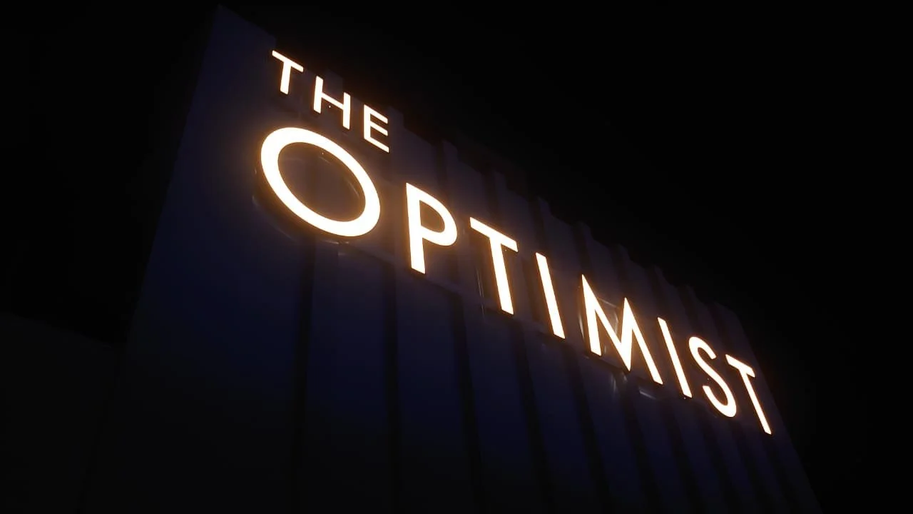 Backlit sign displaying the words 'The Optimum' at night.
