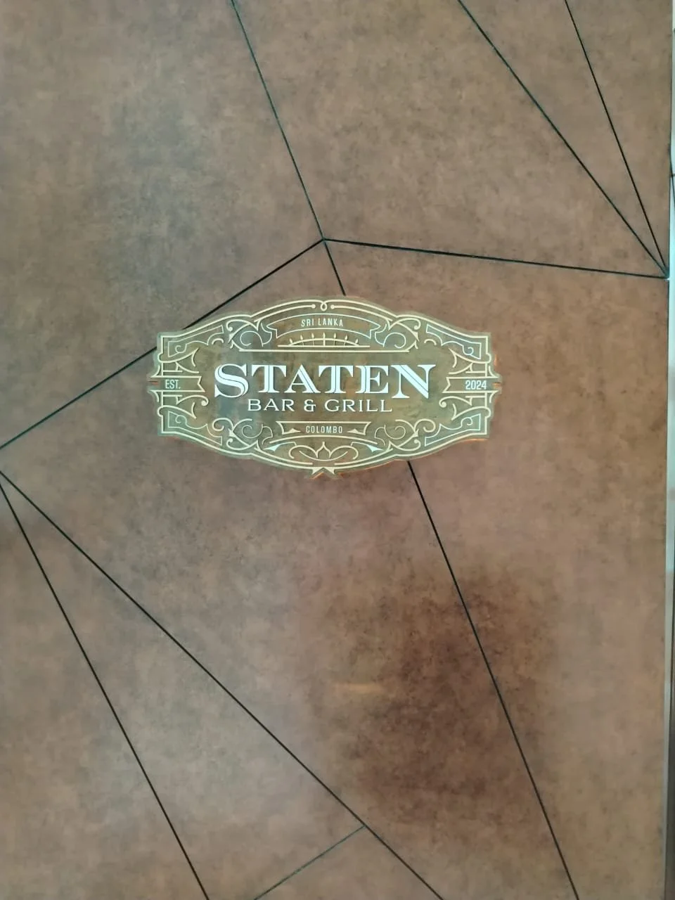 Sign for Staten Bar & Grill in Colombo, Sri Lanka, with decorative border and information about establishment year 2024.