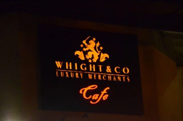 Illuminated sign with the name 'Whight & Co Luxury Merchants Cafe' and a lion crest logo at the top.