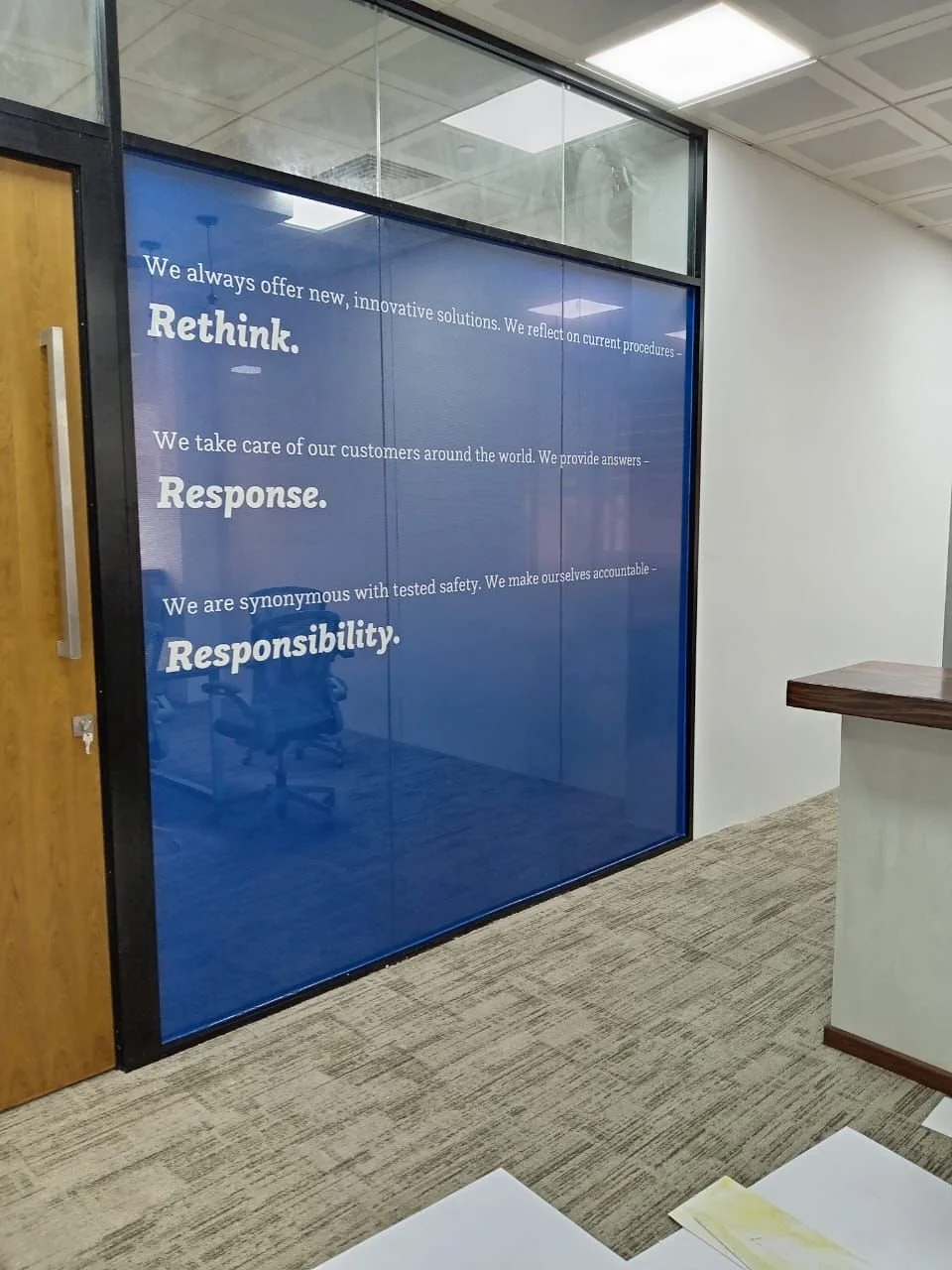 Office interior with a large blue wall graphic featuring motivation and company values about innovation, customer care, safety, and responsibility.