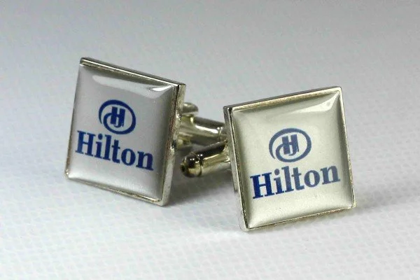 A pair of square Hilton hotel logo cufflinks on a white surface.