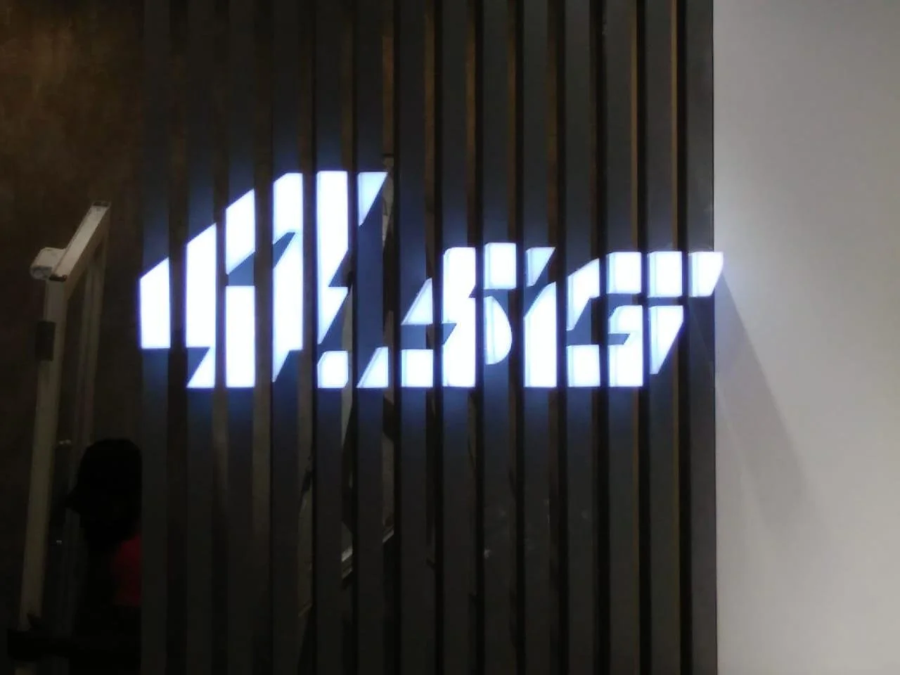 An illuminated digital clock displaying 04:45:12 mounted on dark wooden slats.