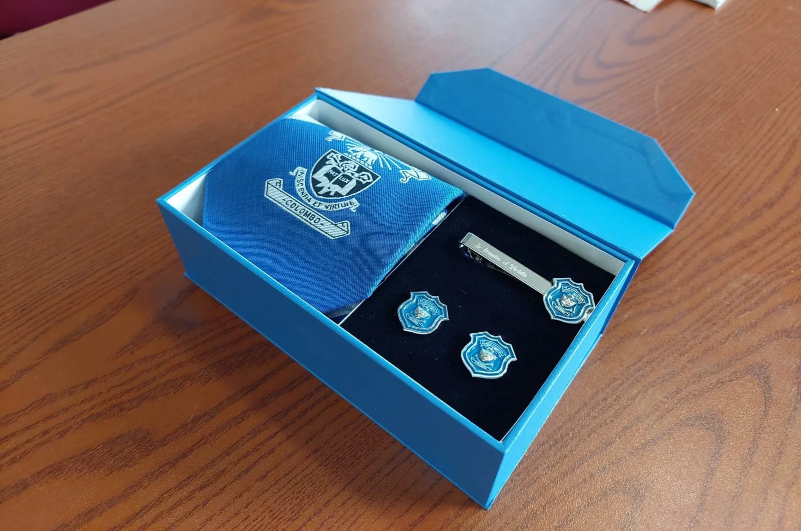 A blue gift box containing police-themed memorabilia, including a tie, patches, and a small badge, all with police insignia, placed on a wooden surface.