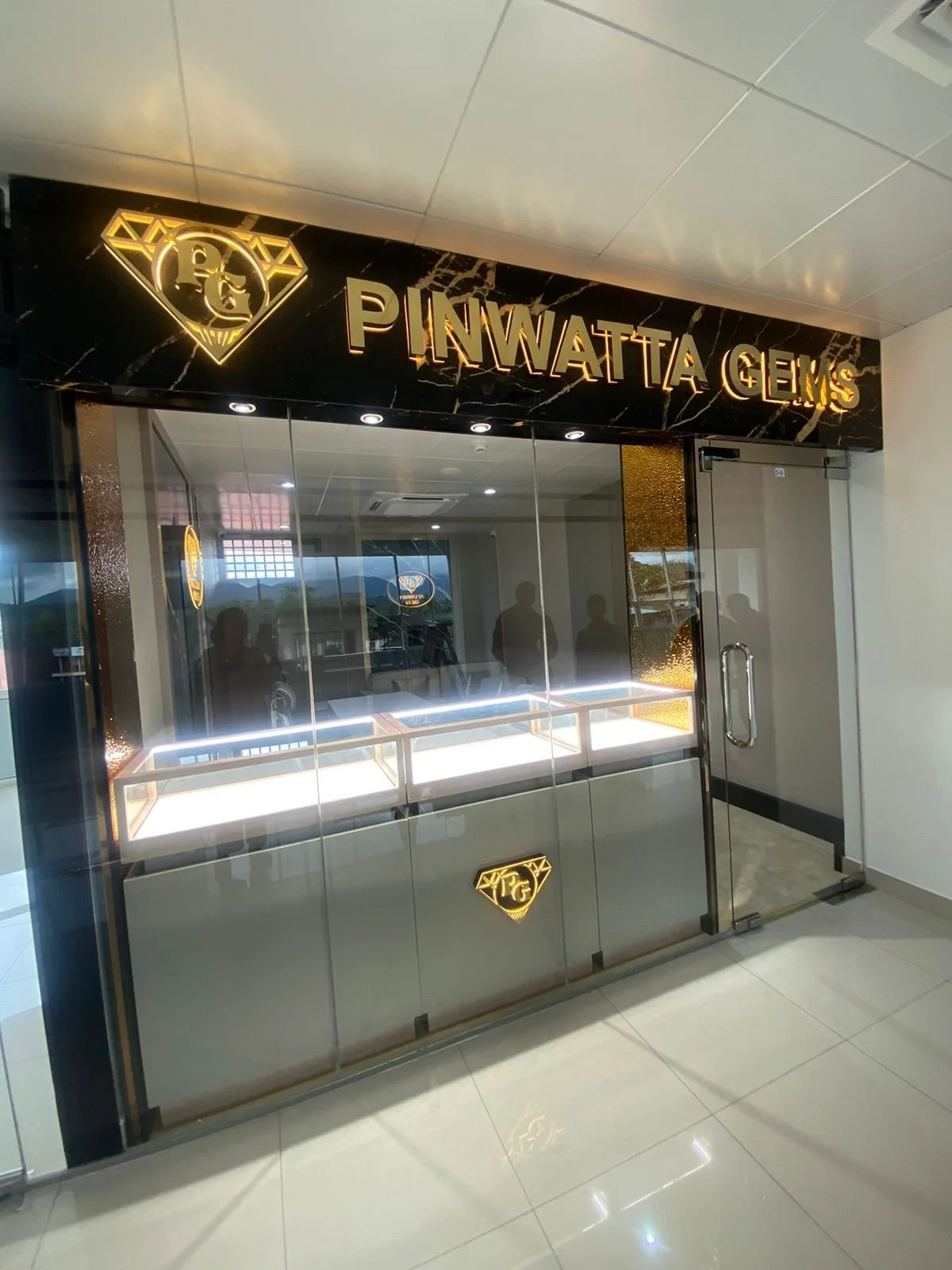 Storefront display for Pinwatta Gems storefront with a black marble sign, gold lettering, and illuminated display cases inside.