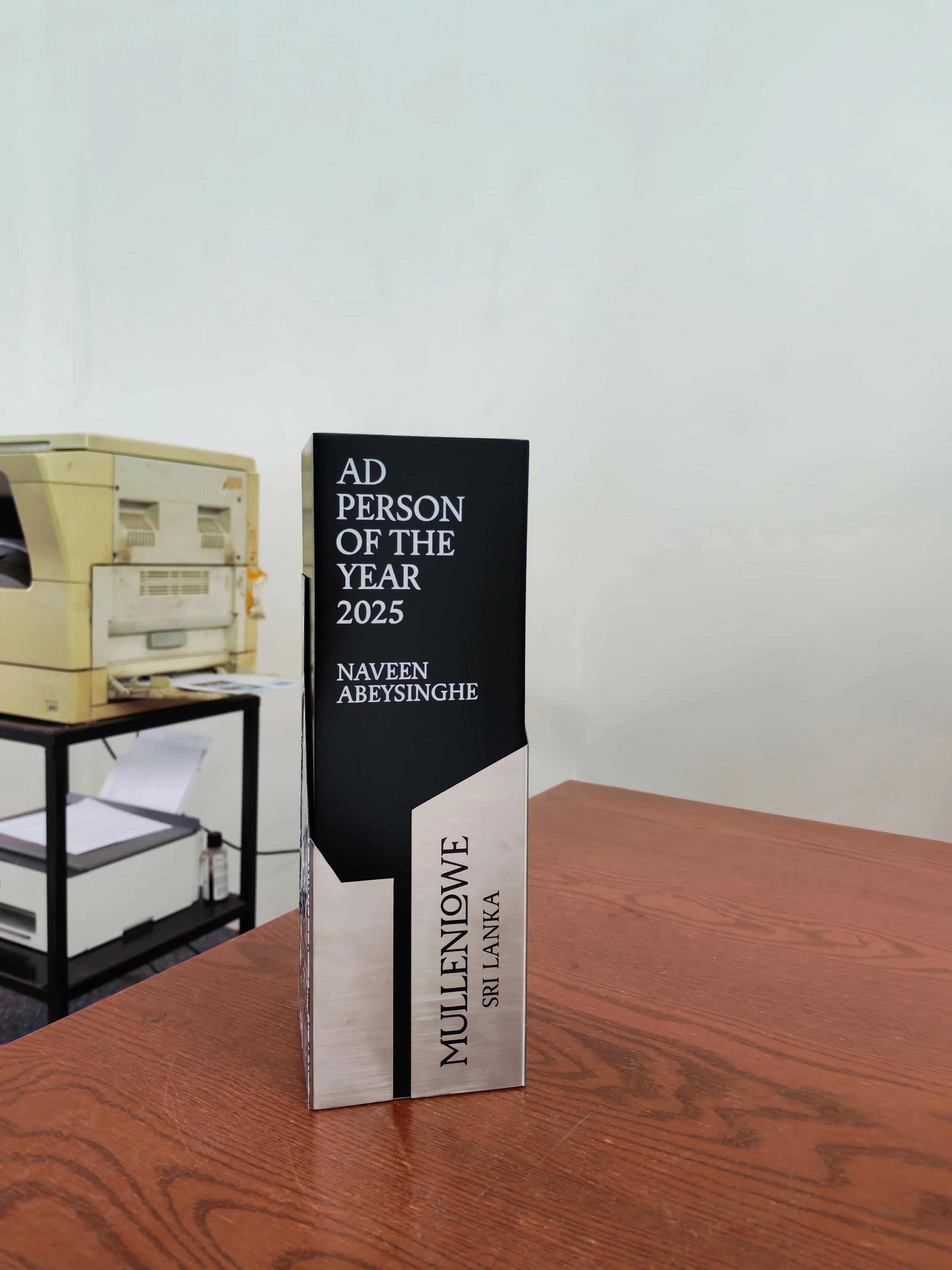 A metallic award trophy featuring black text on a black and white background, sitting on a wooden table in an office or conference room.