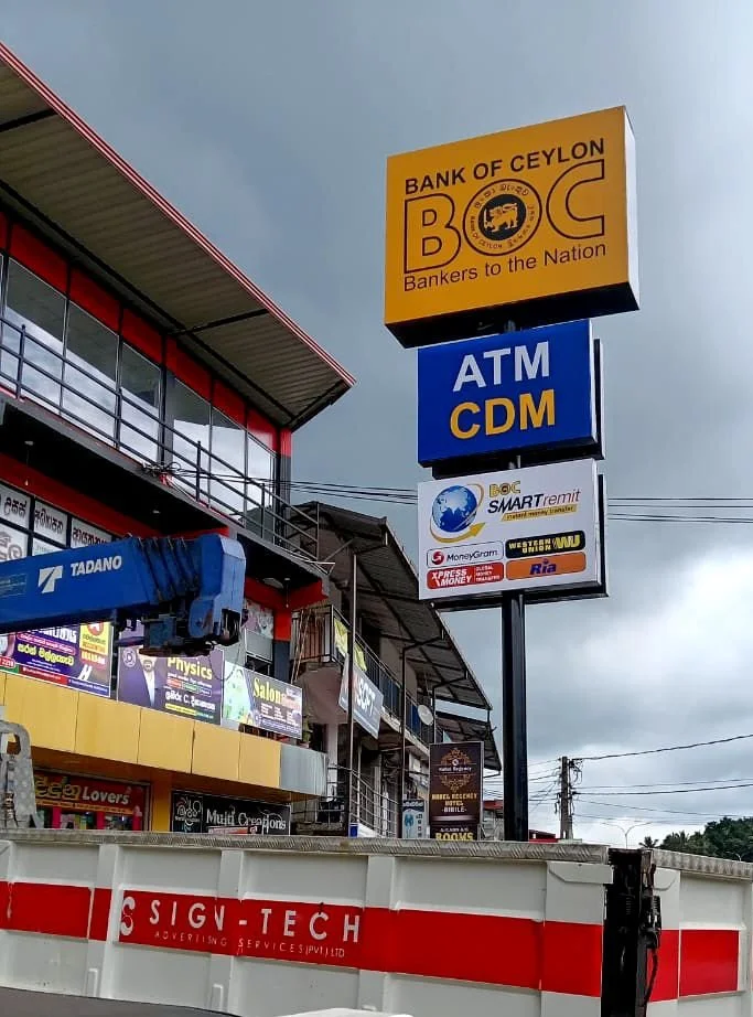 Signboard for Bank of Ceylon with ATM CDM at a commercial area, surrounded by various signs and advertisements.